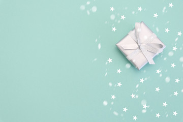 Banner of gifts or present boxes in silver with silver bows and tree ball ornaments and little silver stars, table top view, snowflakes. Composition for Christmas. Turquoise pastel background.