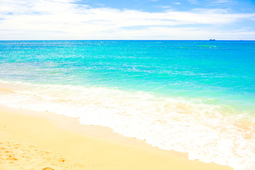 Fototapeta na wymiar Clear blue ocean water coming onto sandy beach with seafoam