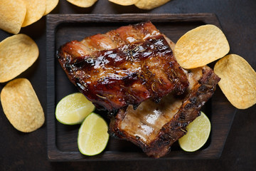 Wooden serving tray with roasted pork ribs glazed in honey and soy sauce, top view, studio shot