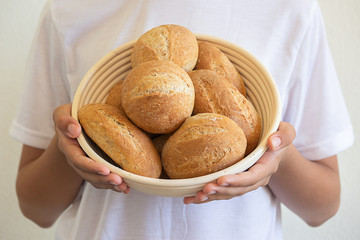A person holds in his hands a basket with small round and oval home-made breakfast buns, daylight...