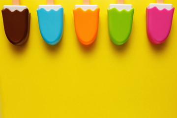 Colorful and various plastic toys ice cream with numbers for babies on a yellow background. Layout. Empty space for the text. Minimalism