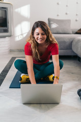 woman doing sports on a mat following online classes with laptop at home