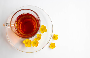 A glass Cup on a saucer with flower tea and yellow flowers stands on a white background. The concept of tea, retro style.Space for your text