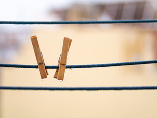 A couple of wooden clothespins on a blue rope with hanging waterdrops after the rain on blurred background. Wet clothesline with clothes clips with copy space.