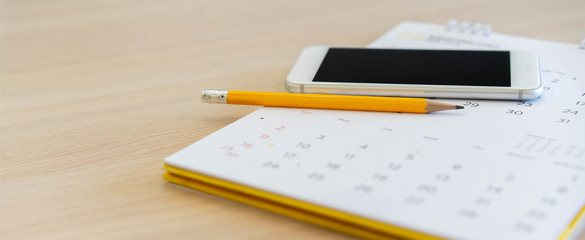 close up on yellow pencil with smartphone on calendar at home office table for appointment and meeting organizer concept