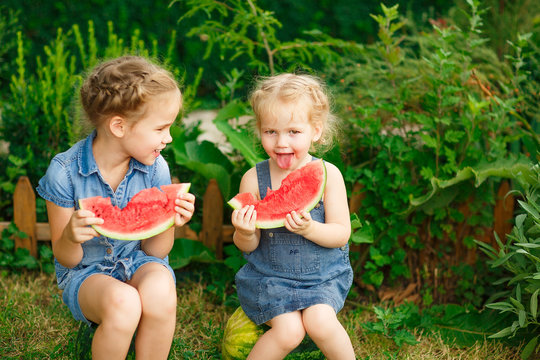 Little girls sit on watermelon and eating pieces 