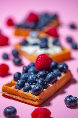 Sweet Homemade waffles with fresh raspberries, blueberries and cream  on pink background 