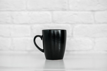 black mug on a white table against a white brick wall