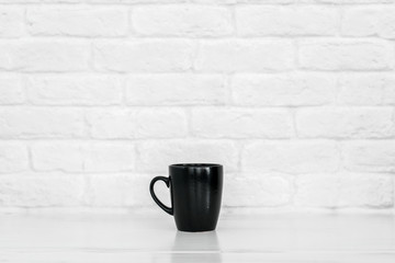 black mug on a white table against a white brick wall