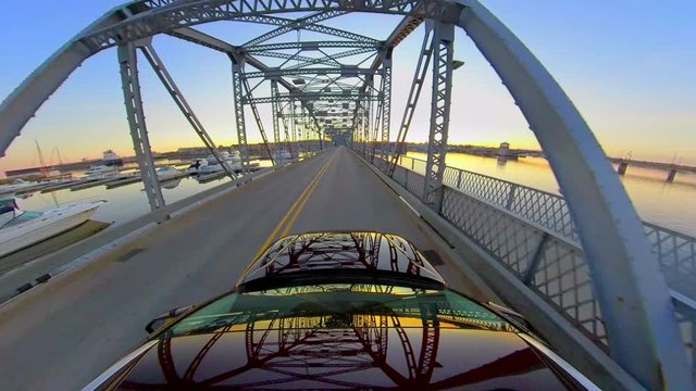 Driving across old style bascule bridge at dawn with wonderful reflections in car top and windshield.