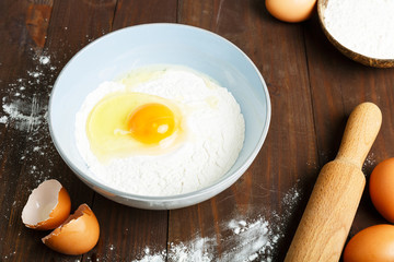 Homemade pasta step by step cooking process. Step 1. flour and broken egg in a blue bowl on a wooden background, eggs, rolling pin.