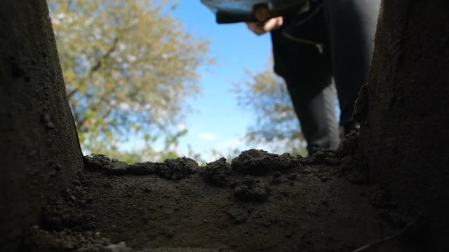 An unrecognizable person in dark clothes is digging a square pit against a blue sky with clouds. Point of view from the grave into which soil is sprinkled from shovel.  Slow motion 200 fps

