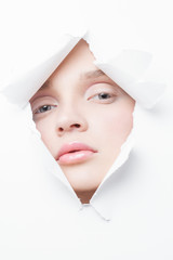 the face of a young beautiful girl with a bright make-up peeks into a hole in paper.