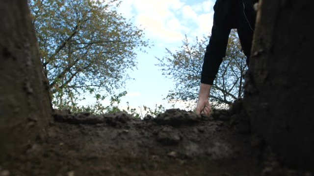 A hand of unrecognizable person in dark clothes throwing the first handful of earth into the grave against a blue sky with clouds. Point of view from the coffin funeral.  Slow motion 200 fps
