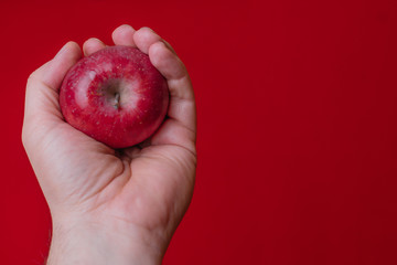 Red apple held by hand with red background.