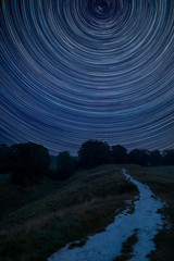 Digital composite image of star trails around Polaris with Stunning inspirational Summer landscape image over English countryside with mist hanging in fields