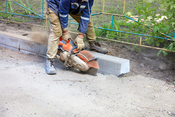 A construction worker using a portable cutter cuts asphalt to repair a worn section of the roadway.