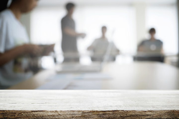 Empty wooden desk space over blurred office or meeting room background. Product display.