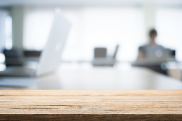 Empty wooden desk space over blurred office or meeting room background. Product display.
