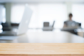 Empty wooden desk space over blurred office or meeting room background. Product display.