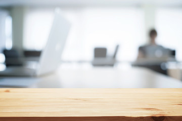 Empty wooden desk space over blurred office or meeting room background. Product display.
