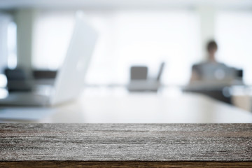 Empty wooden desk space over blurred office or meeting room background. Product display.