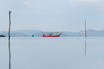 Long tail boat and fisherman in a sea bay with calm water on a background of mountains at sunrise in summer