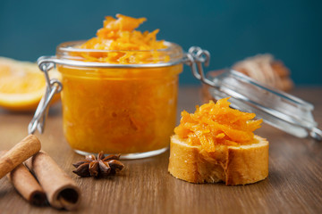 A jar of orange confiture with piece of French baguette, cinnamon and star anise on the wooden background