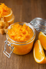 Fototapeta na wymiar A jar of orange confiture, slices of orange fruit, pieces of French baguette on the wooden background