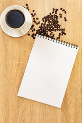 Obraz na płótnie Canvas vertical photos, on the table there is a mug with aromatic coffee, coffee grains near a cup on the surface, a sheet of paper for writing ideas
