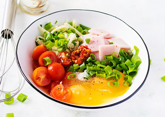 Omelette ingredients: eggs, ham, tomatoes, green herbs, milk and cheese on the light table.