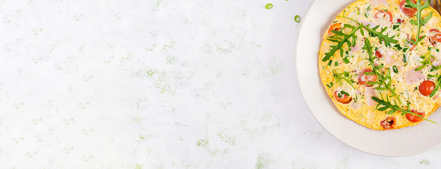 Omelette with tomatoes, ham, cheese and green herbs on plate.  Frittata - italian omelet. Top view, overhead, copy space