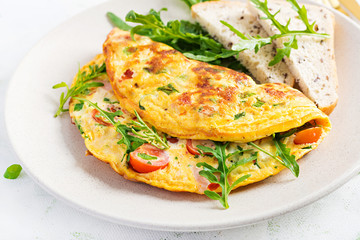 Omelette with tomatoes, ham, cheese and green herbs on plate.  Frittata - italian omelet.