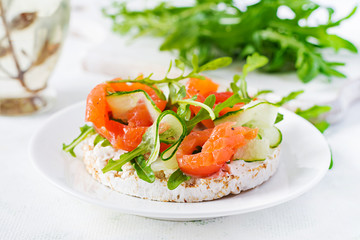 Open sandwich with  crispbread salted salmon, cream cheese, sliced cucumber and arugula on plate.