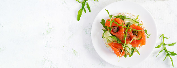 Open sandwich with  crispbread salted salmon, cream cheese, sliced cucumber and arugula on plate. Top view, overhead, copy space