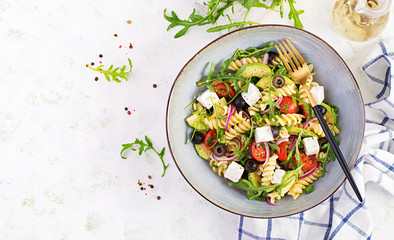 Pasta salad with tomato, avocado, black olives, red onions and cheese feta. Mediterranean cuisine. Top view, overhead, flat lay