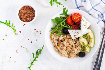 Breakfast oatmeal porridge with greek salad of tomatoes, avocado, black olives and arugula. Healthy balanced food. Top view, flat lay, copy space