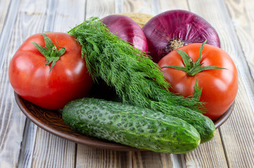 On a plate are vegetables, tomatoes, cucumbers, onions and dill. Fresh vegetables close-up. Natural food.