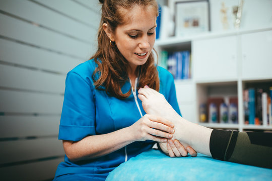 Girl physiotherapist treating her client's foot while smiling. Physiotherapist in his professional clinic.