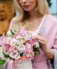 Portrait of a young attractive blonde woman with a bouquet of flowers in a hat box. Pale pink spring flowers with a ribbon. March 8, International Women's Day