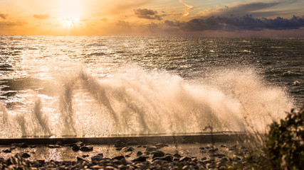 Rozbijające się fale morza Bałtyckiego o brzeg podczas sztormu w zachodzącym słońcu.