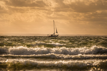 Żaglówka, jacht na morzu podczas zachodu słońca na spienionych falach. © Artur Wojtczak 
