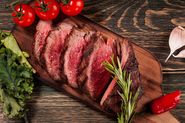 Sliced of roast beef appetizer with rosemary and tomatoes, wood background top view.