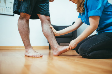 Physiotherapist stretching the foot of a young client. Blue and white physiotherapy clinic