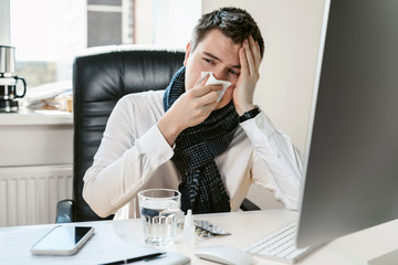 A young freelancer, businessman or office worker sneezes, coughs, blows his nose at the workplace. Overworked worker got colds and flu. High temperature with ARVI. Epidemic of influenza or coronavirus