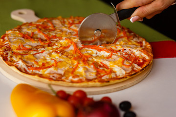 Cutting a baked pizza on slices. Close-up cutter knife.