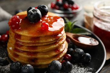 Plate of tasty pancakes with berry and powder on wooden table. Composition of sweet breakfast