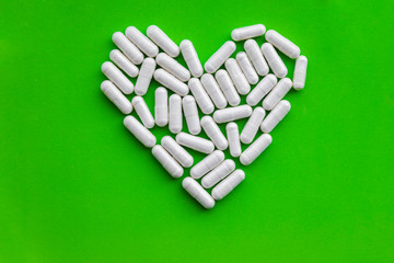 Heart shape of white vitamin supplements, loving health dietary capsule pills on bright green background with copy space