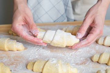 A woman is cooking croissants. Prepare for baking. Delicious traditional french crispy croissants for breakfast. Homemade bakery, cuisine for family. Girl chef work on kitchen table. Raw croissants