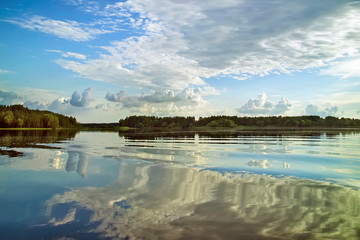 Volga river. On the horizon, you can see wooded banks. The blue sky with white clouds is reflected in the water.